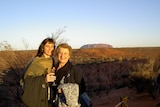 Elderly woman with her daughter standing with Uluru in the background.