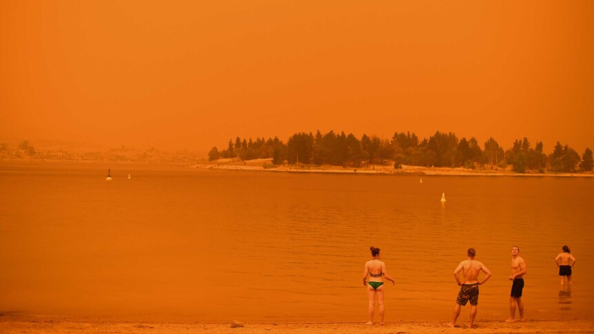 Swimmers standing on Jindabyne lake with a red smoky sky