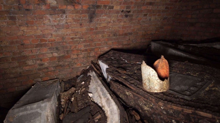 A red and gold mitre sits on top of a coffin in an underground tomb.