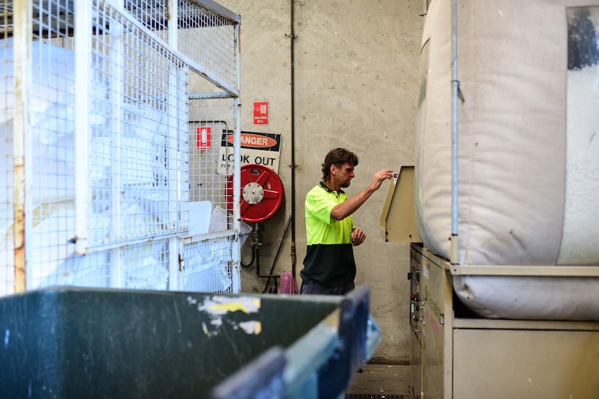 Man in distance attends to some machinery, there's a storage cage to his left.