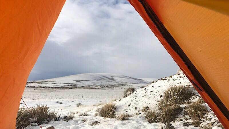A snowy landscape as seen through tent flaps.