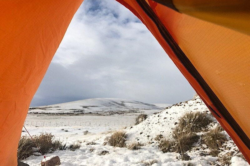 A snowy landscape as seen through tent flaps.