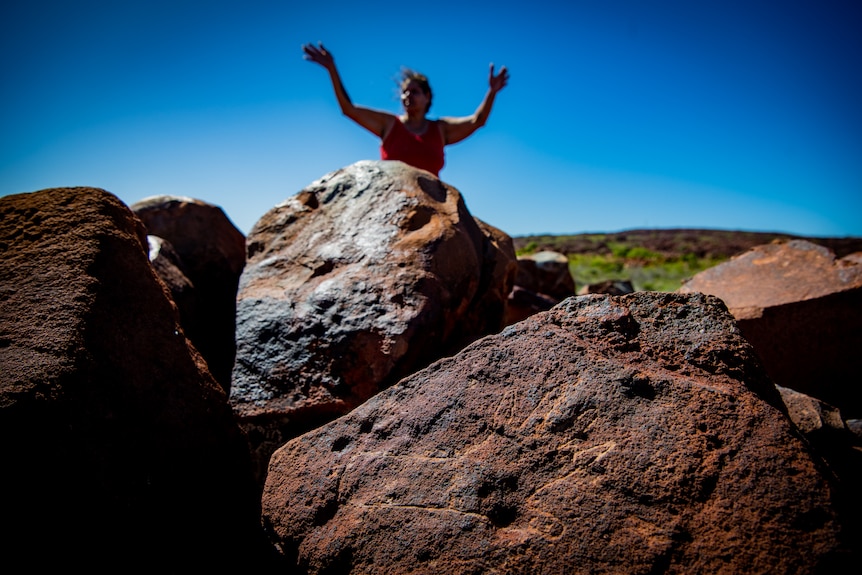 Raelene Cooper waves her hands in the air while standing on the rocks in the Burrup Peninsula.