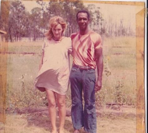 Megan's mum and dad standing together, arms around each other, trees and grass behind.