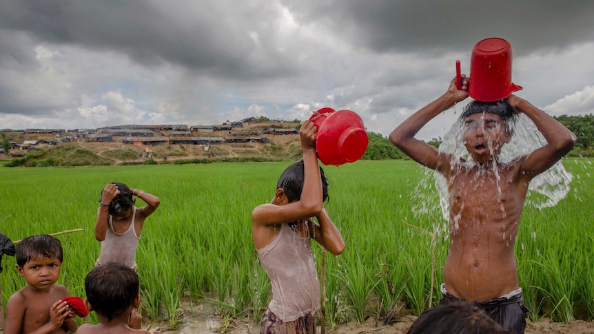 Children are pouring buckets of water on themselves near a paddy field in Bangladesh.