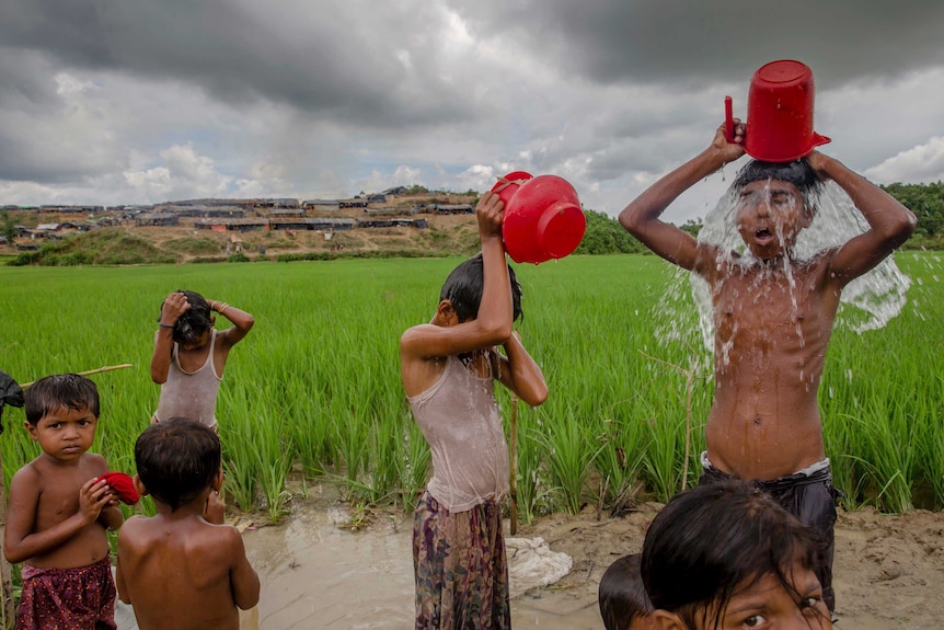 Children are pouring buckets of water on themselves near a paddy field in Bangladesh.