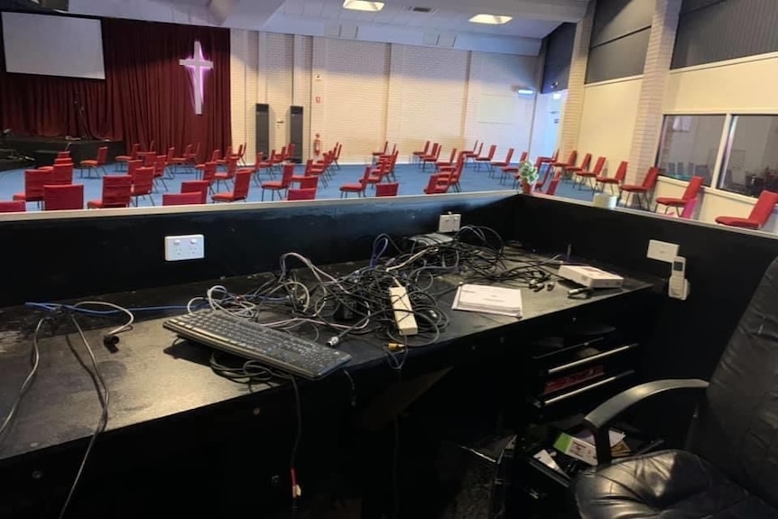 Tangles of cords o a table with spaced out chairs behind and a cross