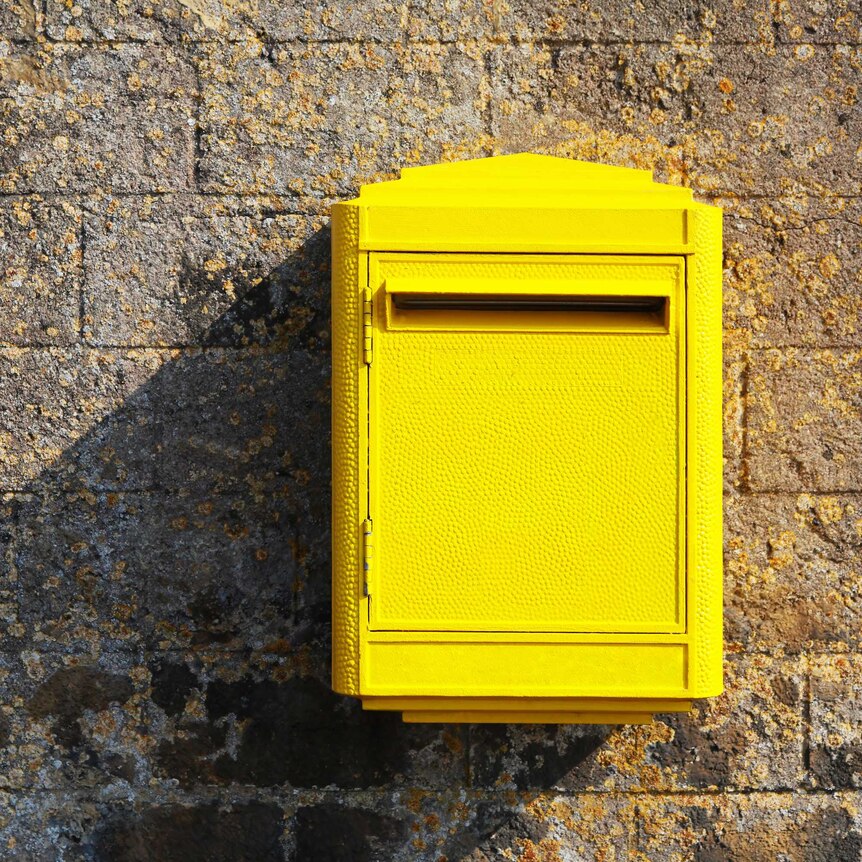 Yellow postbox in front of stone wall.