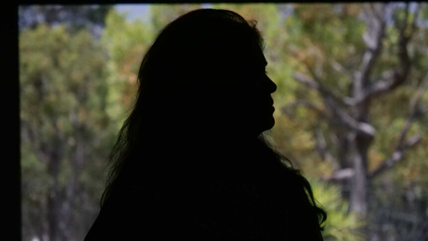 A silhouette of a woman with trees behind her.