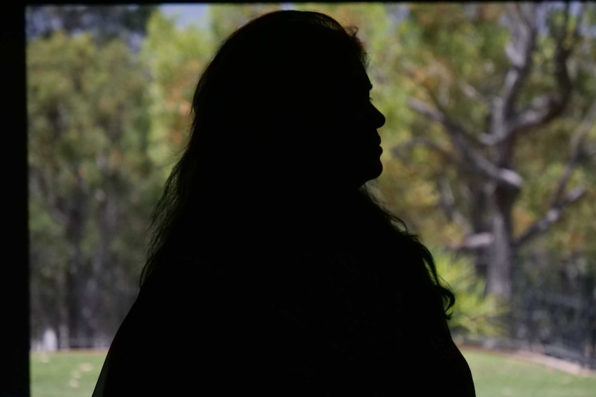 A silhouette of a woman with trees behind her.