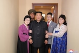 a group of four people stand around and hug Kim Jong Un in the doorway of one of a new residential terrace