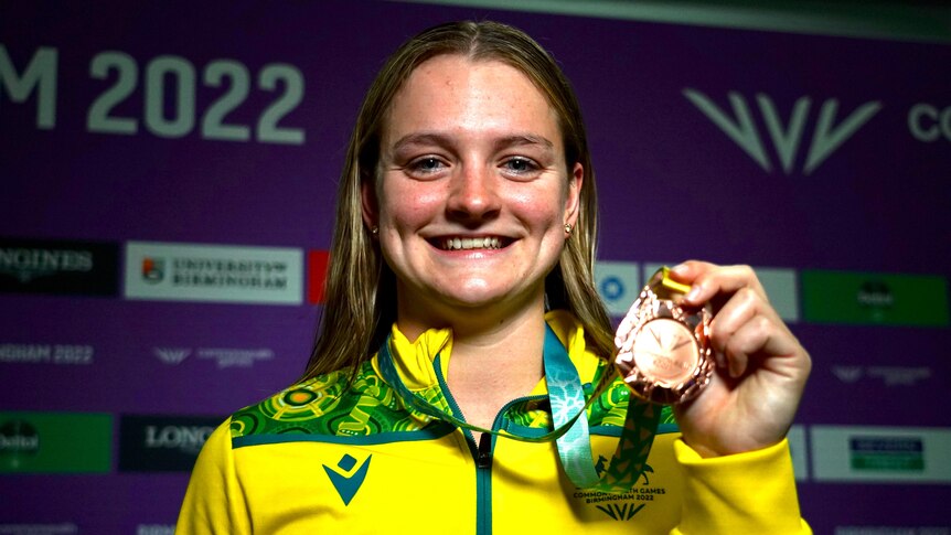swimmer chelsea hodges smiles while holding up her commonwealth games bronze medal