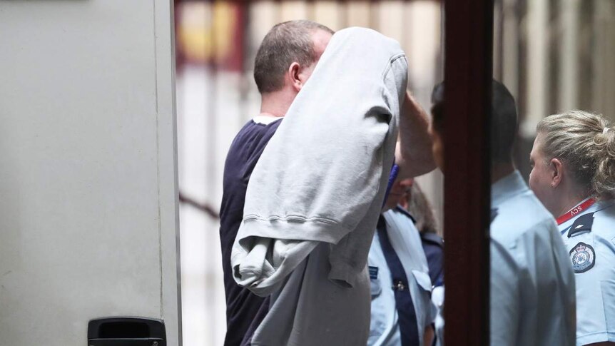Scott Murdoch wears a grey jumper over his head as he is led from a prison van into court.