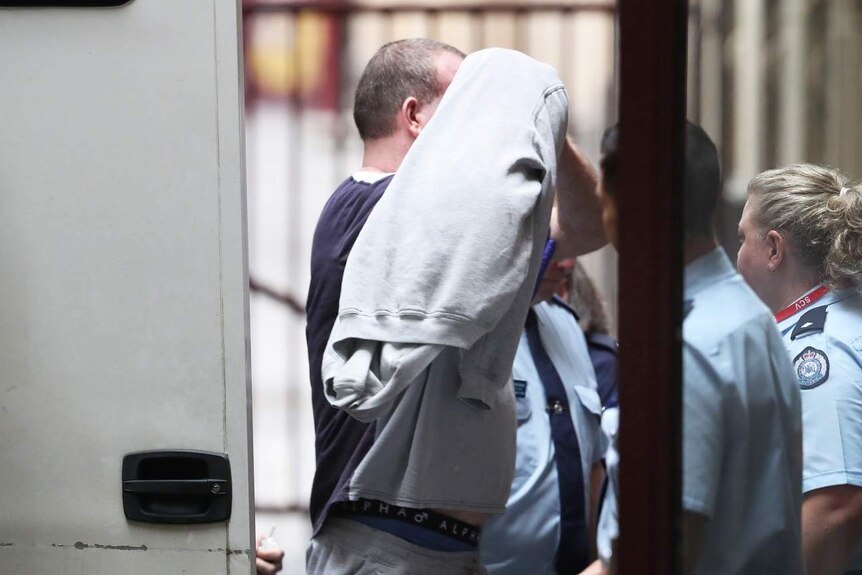 Scott Murdoch wears a grey jumper over his head as he is led from a prison van into court.