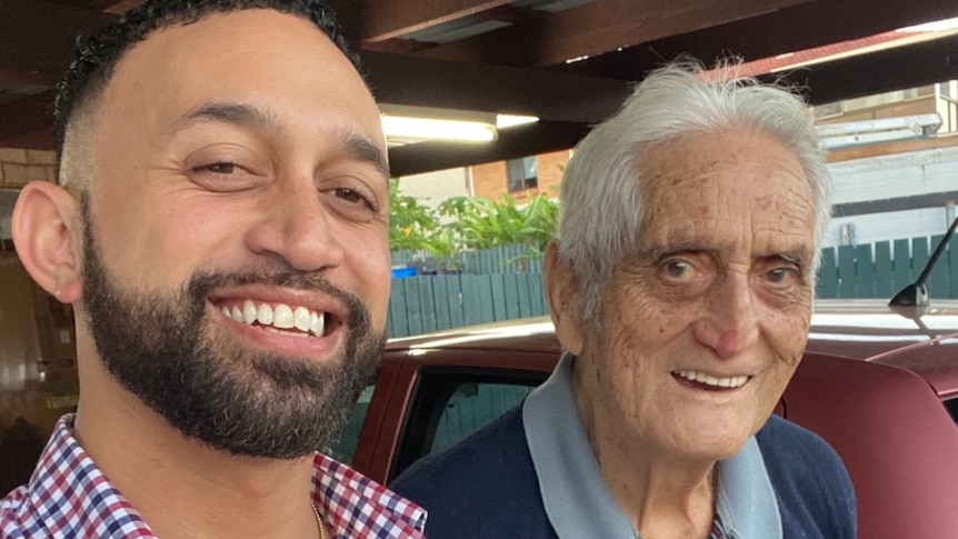 A smiling young bearded man with his grey-haired grandfather. Both are smiling.