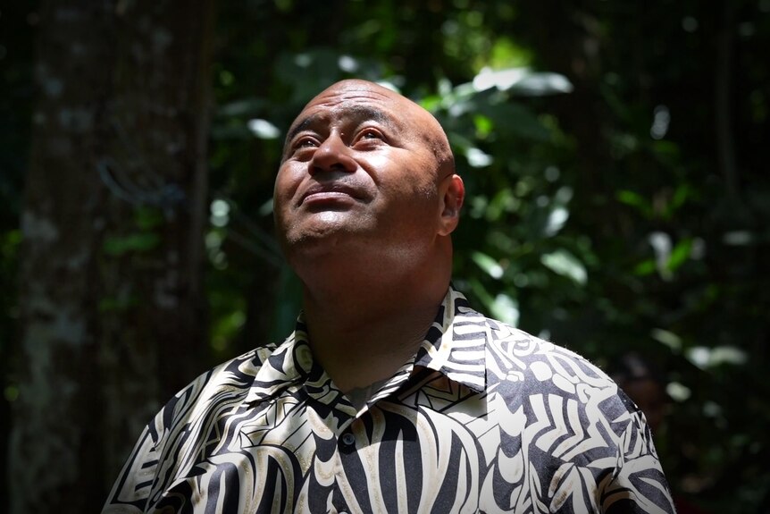 A man wearing an island shirt looks up into a shaft of light.