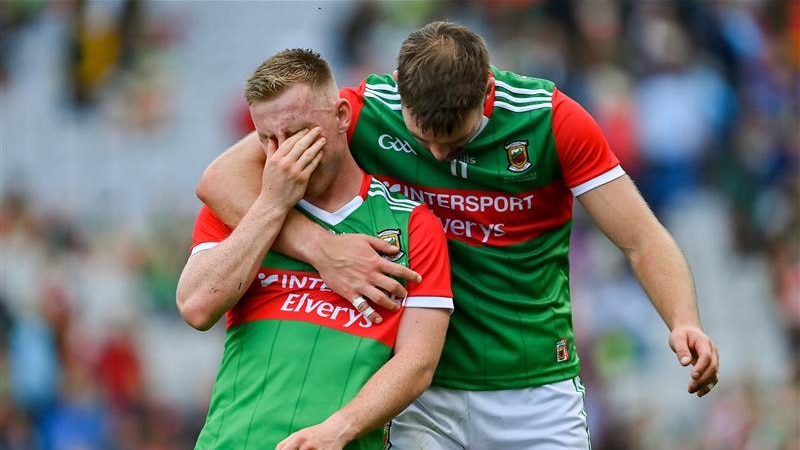 A distressed Mayo footballer puts his hand over his face as his teammate hugs him after an All-Ireland final loss.