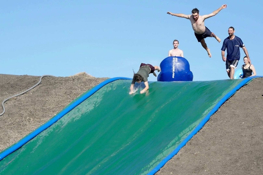 A man takes a running leap on the farm waterslide
