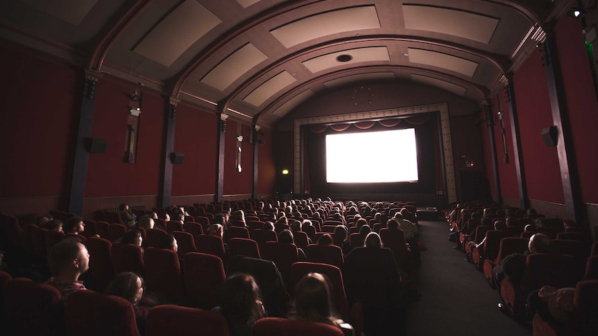 Cinema with audience members looking at a brightly lit screen in a darkened room.