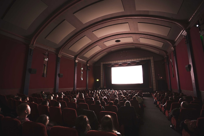 Cinema with audience members looking at a brightly lit screen in a darkened room.