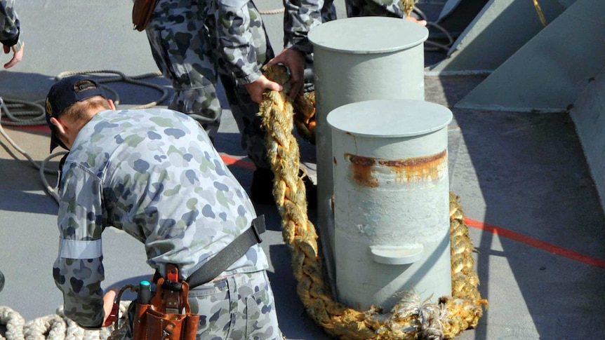 Australian Navy sailors place lines from a tugboat around a bollard.