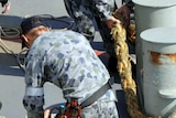Australian Navy sailors place lines from a tugboat around a bollard.