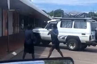 two Indigenous people stand off with fists raised in a car park