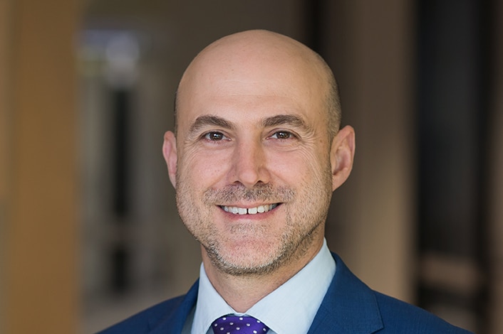 A portrait photo of a smiling man with a bald head wearing a suit.