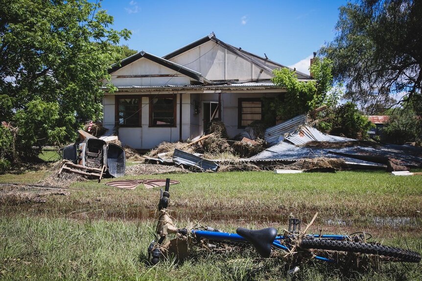 A damaged bike on a lawn in front of a home badly damaged by a flood.