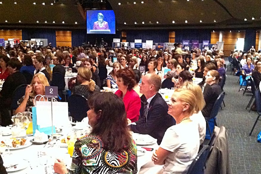 Mr Newman (seated at table) listens as ms Bligh speaks at the IWD breakfast in Brisbane.