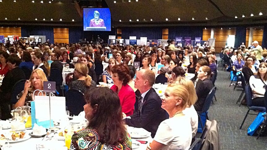 Mr Newman (seated at table) listens as ms Bligh speaks at the IWD breakfast in Brisbane.