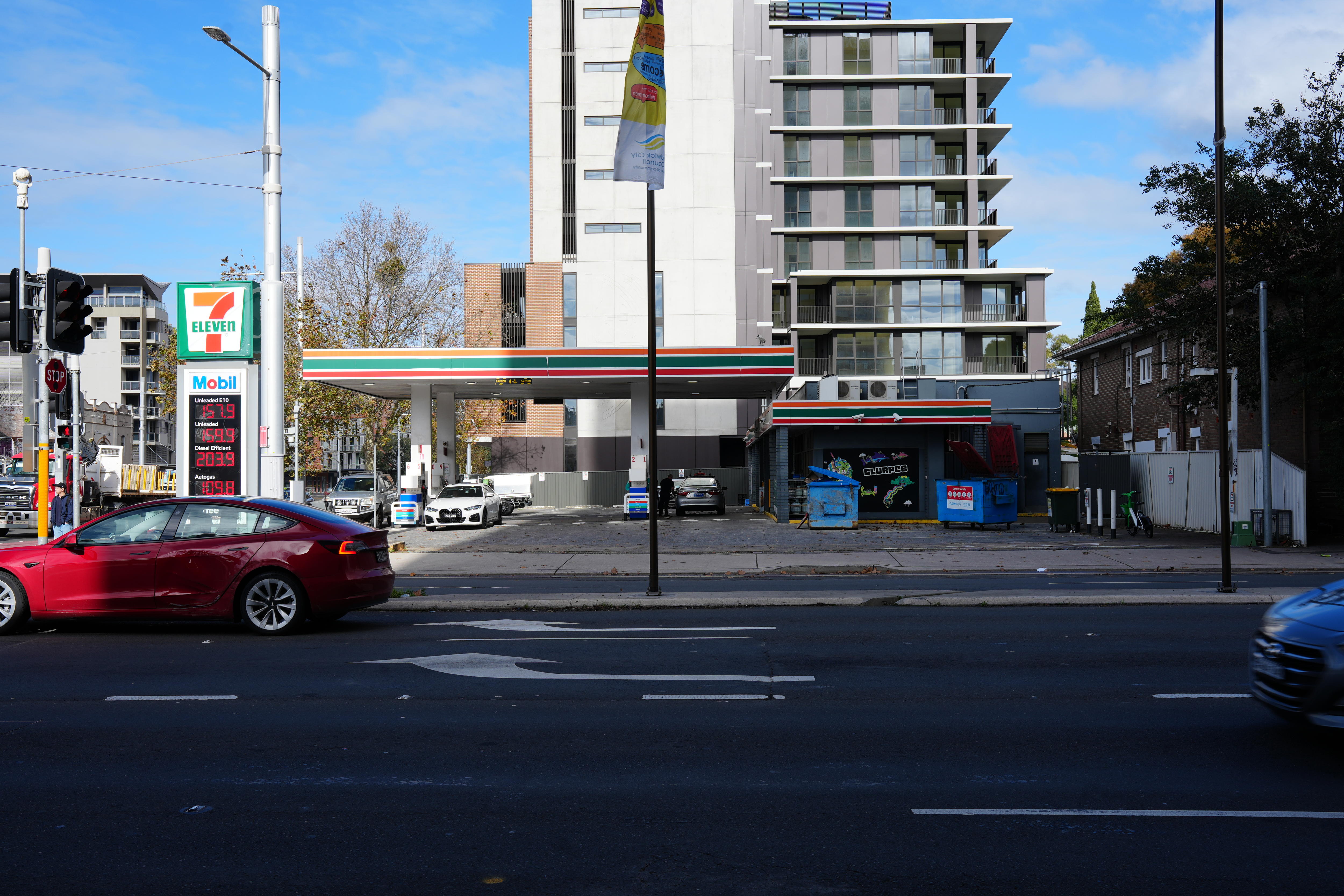 A 7-Eleven petrol station on a city street near a high-rise unit building.