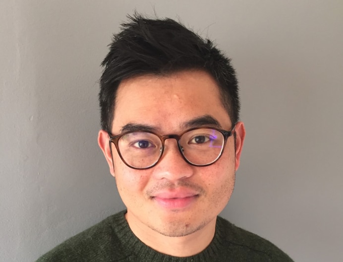 Una foto de perfil de un hombre con gafas, sonriendo sin mostrar los dientes. 