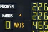 An old-fashioned manual scoreboard that reads "PUCOVSKI 226, HARRIS 226, 0 WKTS 465"
