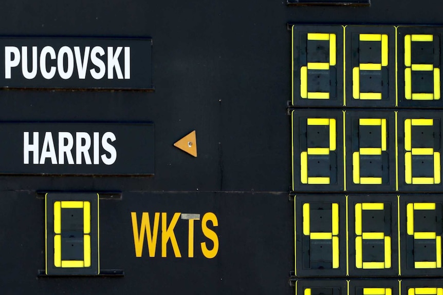 An old-fashioned manual scoreboard that reads "PUCOVSKI 226, HARRIS 226, 0 WKTS 465"