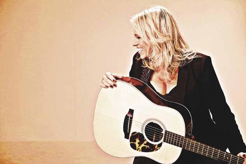 Beccy Cole holding a guitar and looking away from the camera