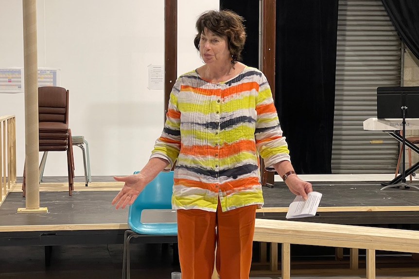 A woman stands with her arms outstretched holding a piece of paper in front of a stage