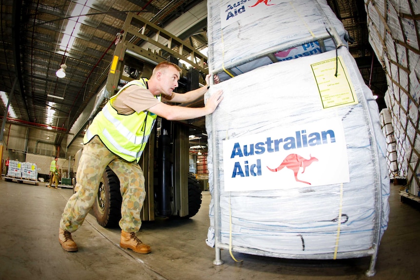 An Australian soldier pushes bundles of aid.