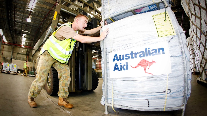 An Australian soldier pushes bundles of aid.