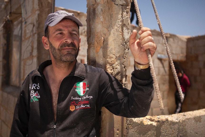 Abdo Kanaan holds onto a steel pole and looks to the left as he stands outside his party torn down house