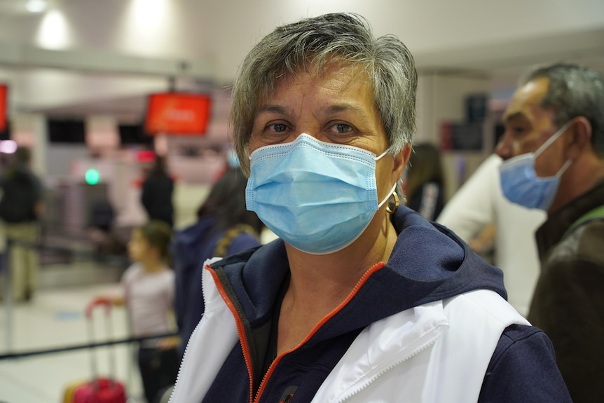 A woman with short salt and pepper hair, wearing a blue surgical mask at the airport. 