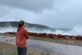 A young man stands on the coast watching the ocean.