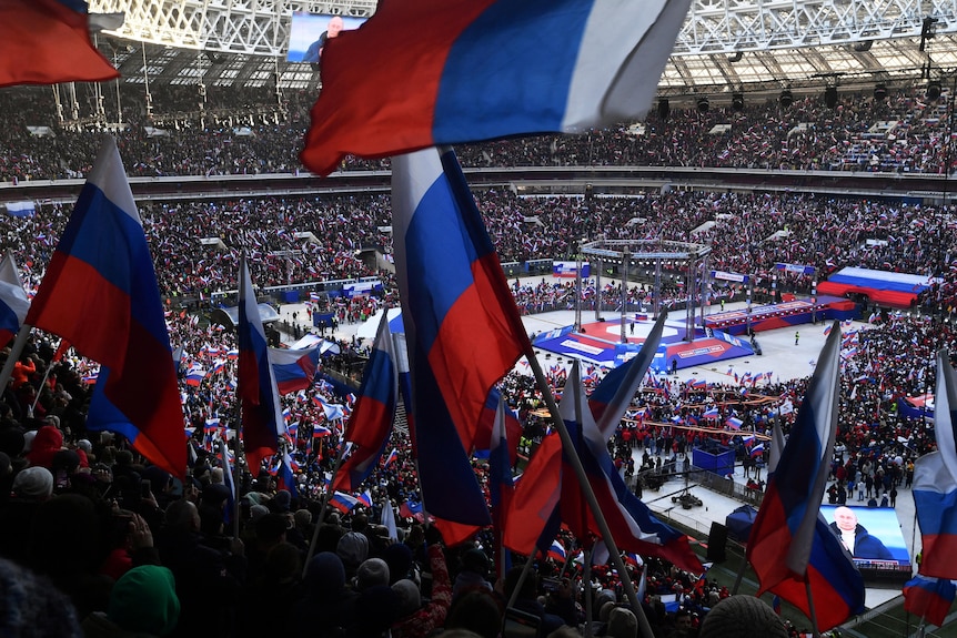 People wave Russian flags at a packed stadium.