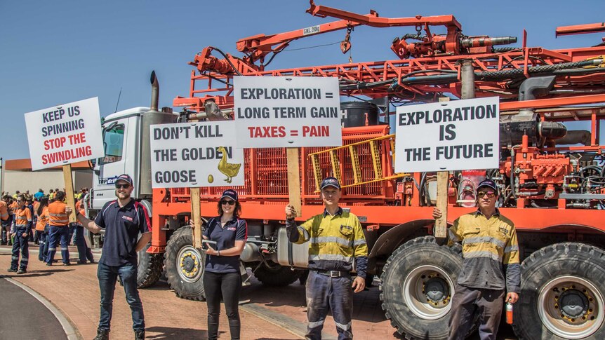 Workers hold signs while standing in front of a drill rig.