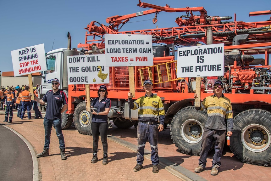 Workers hold signs while standing in front of a drill rig.