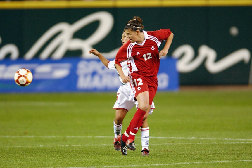 Two female soccer players, one wearing red and another wearing white, during a match