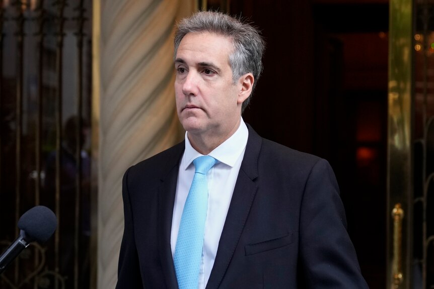 A photo of Michael Cohen on his way to court. He's wearing a blue tie and navy suit. He has short grey hair.
