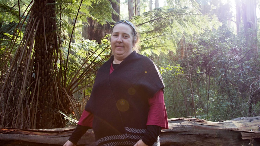 A woman stands next to a felled tree with shield-shaped scar marks.