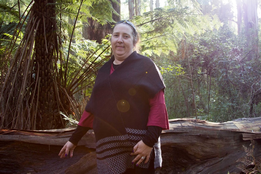 A woman stands next to a felled tree with shield-shaped scar marks.