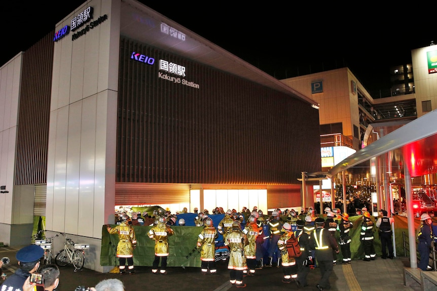 Fire services hold screens to obscure view outside Tokyo train station.